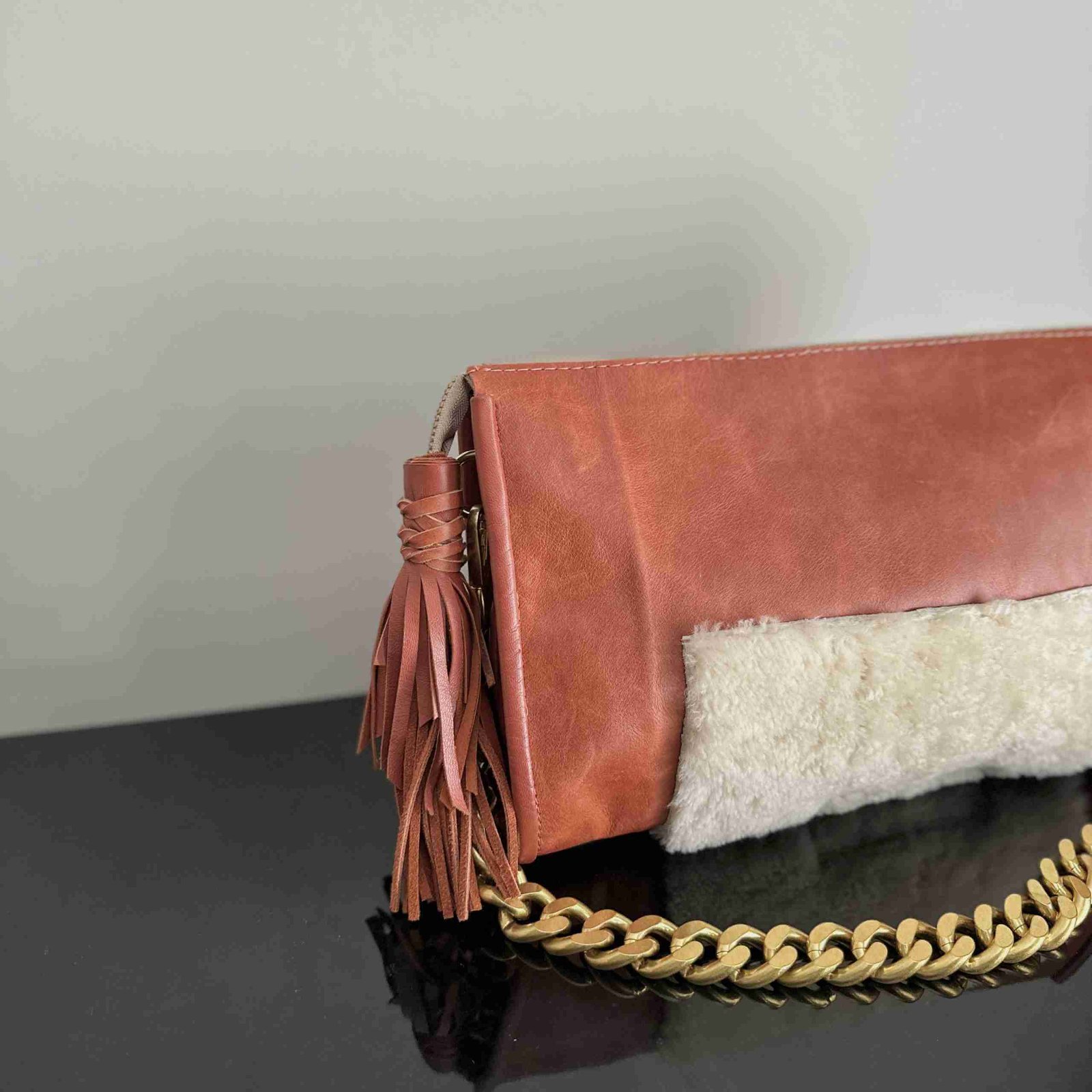Rust leather bag with cream shearling accents, a chunky removable shoulder chain, a tassel zipper detail, and leather lining with an interior pocket.