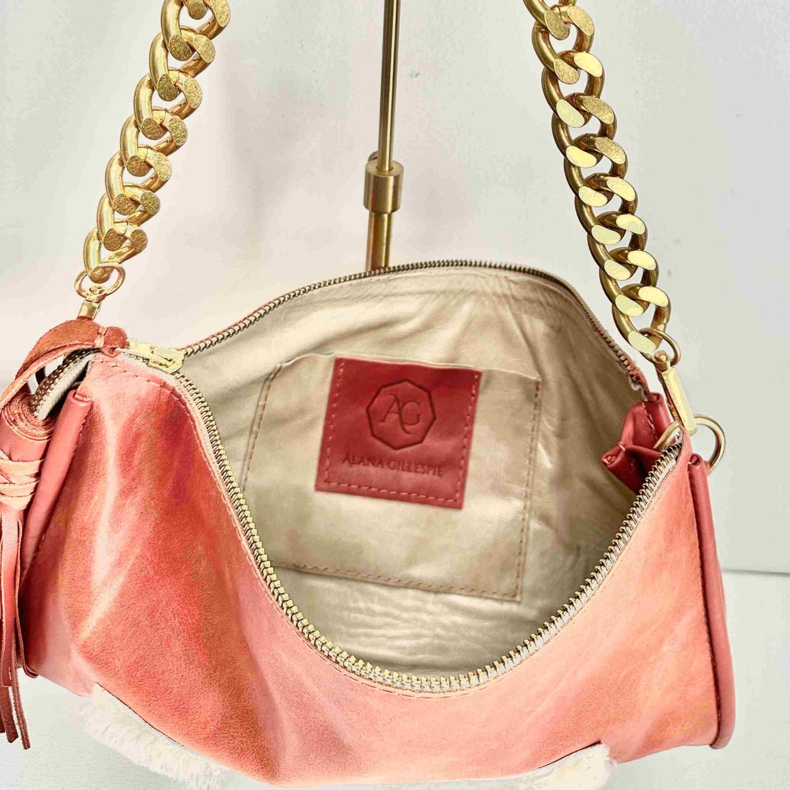 Rust leather bag with cream shearling accents, a chunky removable shoulder chain, a tassel zipper detail, and leather lining with an interior pocket.