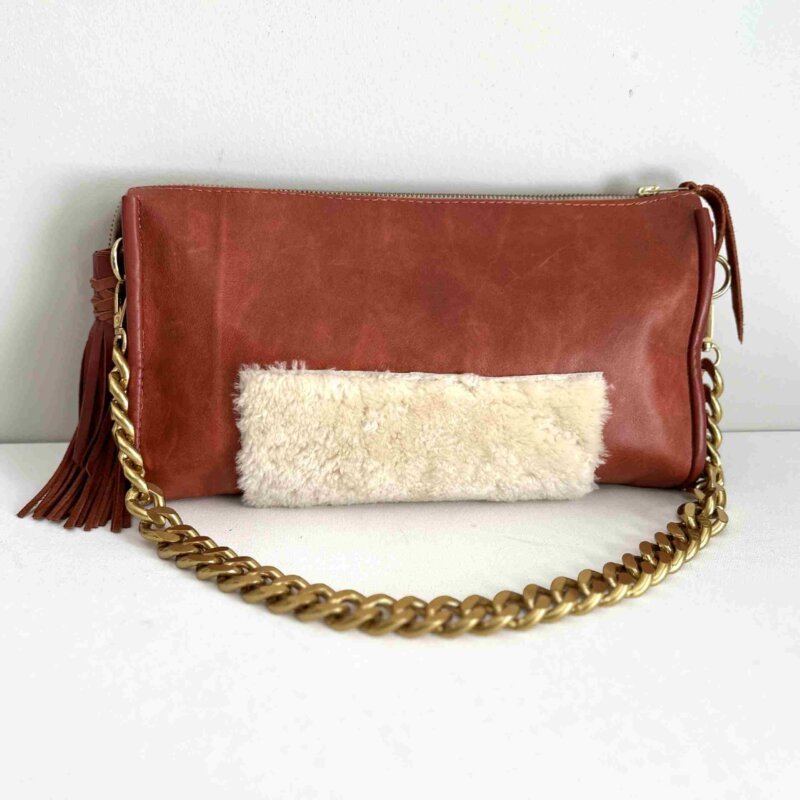 Rust leather bag with cream shearling accents, a chunky removable shoulder chain, a tassel zipper detail, and leather lining with an interior pocket.