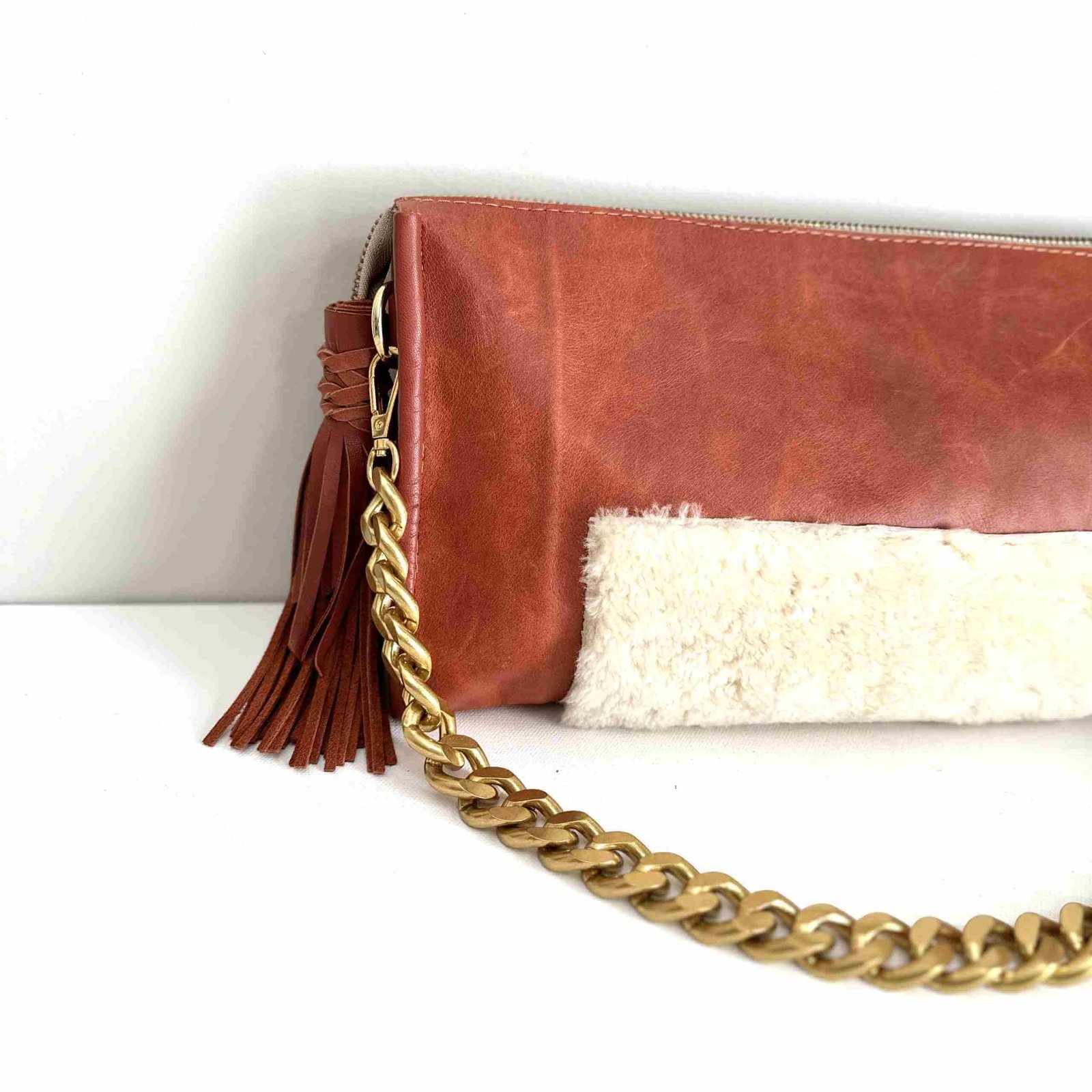 Rust leather bag with cream shearling accents, a chunky removable shoulder chain, a tassel zipper detail, and leather lining with an interior pocket.