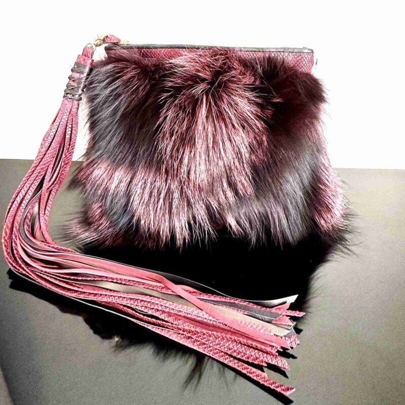 Mercer Fox Fur Clutch Bag with black and magenta fur, brass zipper closure, and magenta lining, displayed on a modern surface.