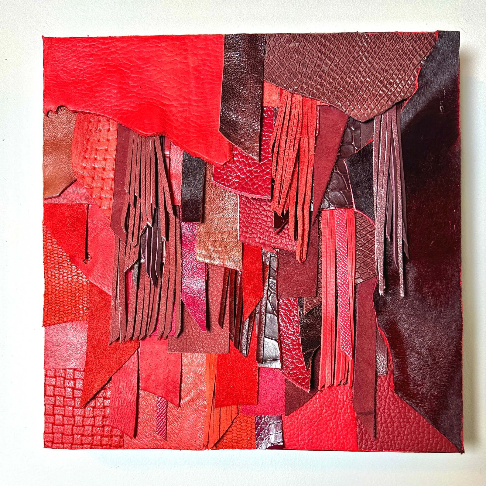 Abstract red leather wall art with layered textures and fringe on wood panel