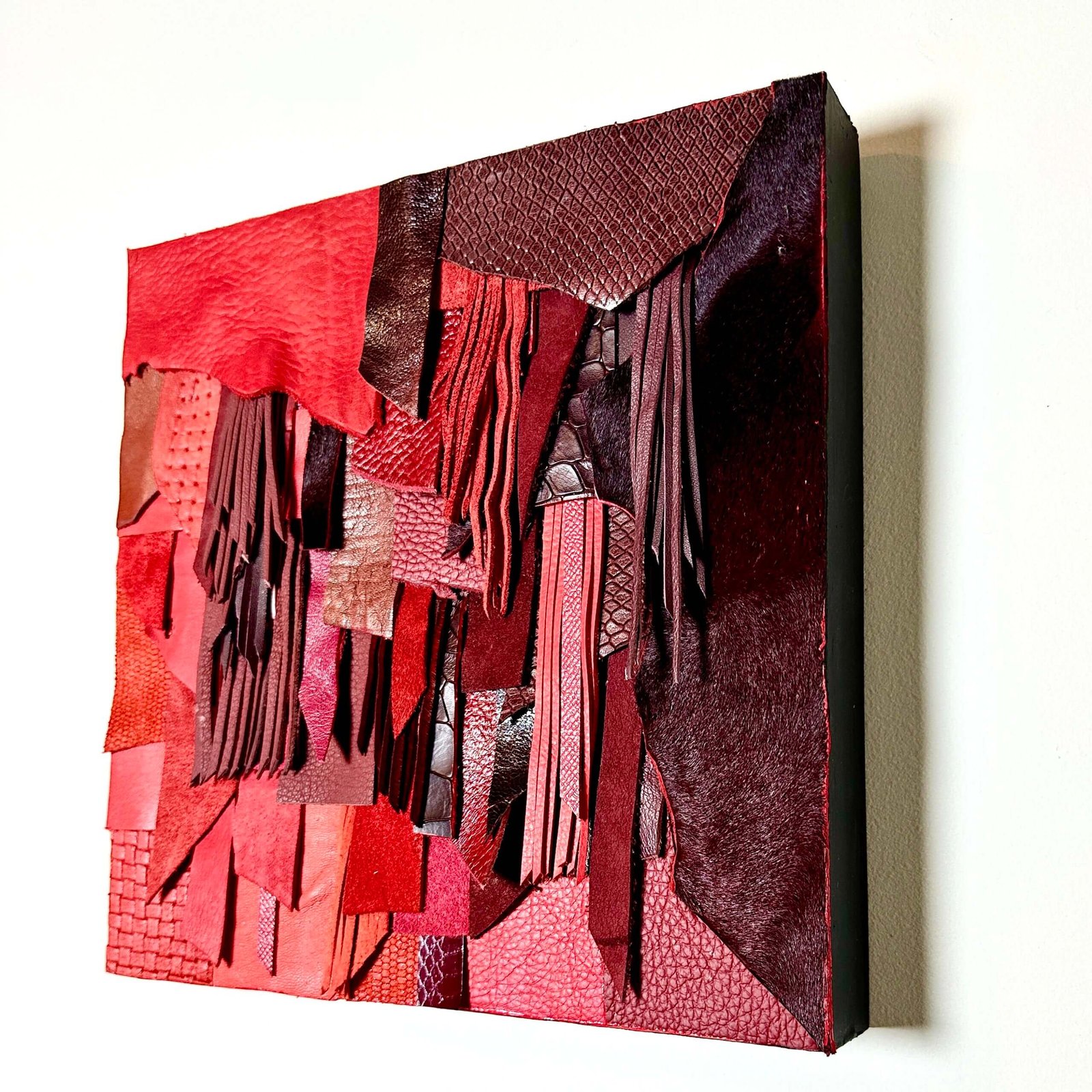 Abstract red leather wall art with layered textures and fringe on wood panel
